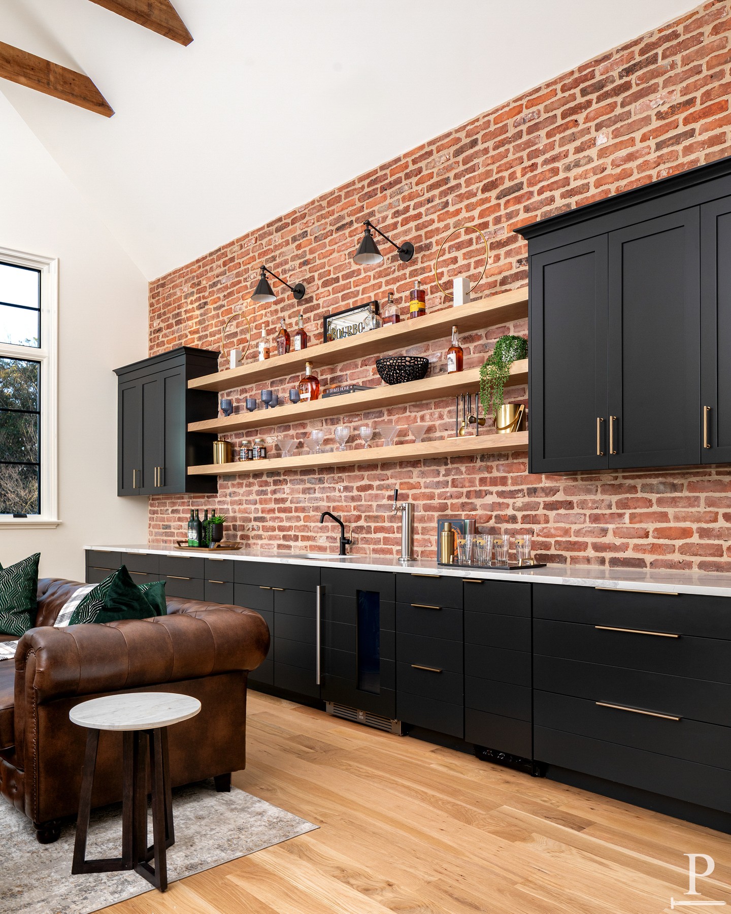 This bonus room bar is the ultimate hangout spot. 🥃 
Exposed brick accent wall, black cabinetry with brass hardware, floating oak shelves, and a beverage fridge stocked and ready. Built for game nights, happy hours, and everything in between.