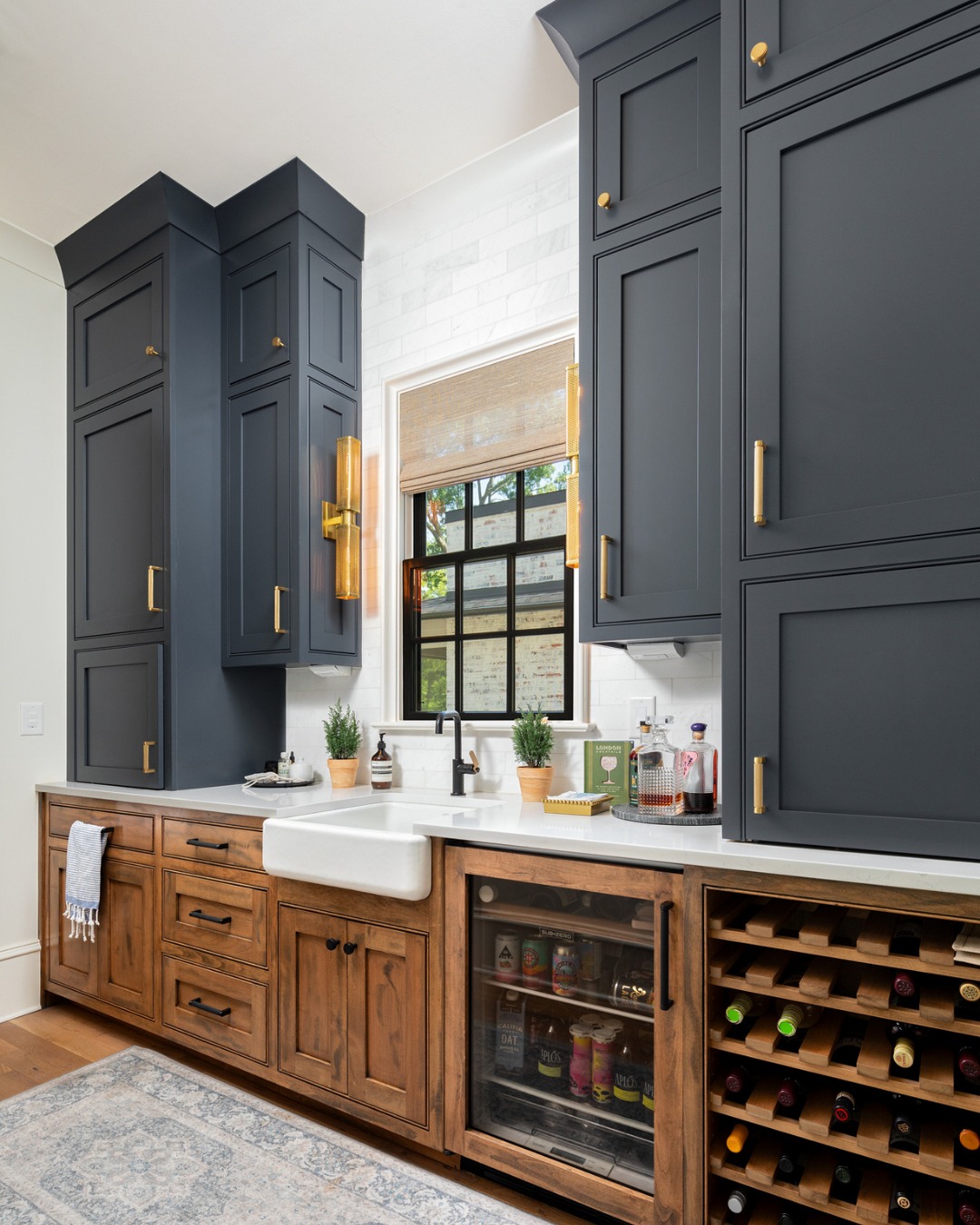 Navy uppers, warm wood lowers, brass in between. This scullery does double duty as the ultimate bar setup, wine storage, beverage fridge, and a farmhouse sink for easy cleanup. The kind of room that makes hosting feel effortless. 🍷