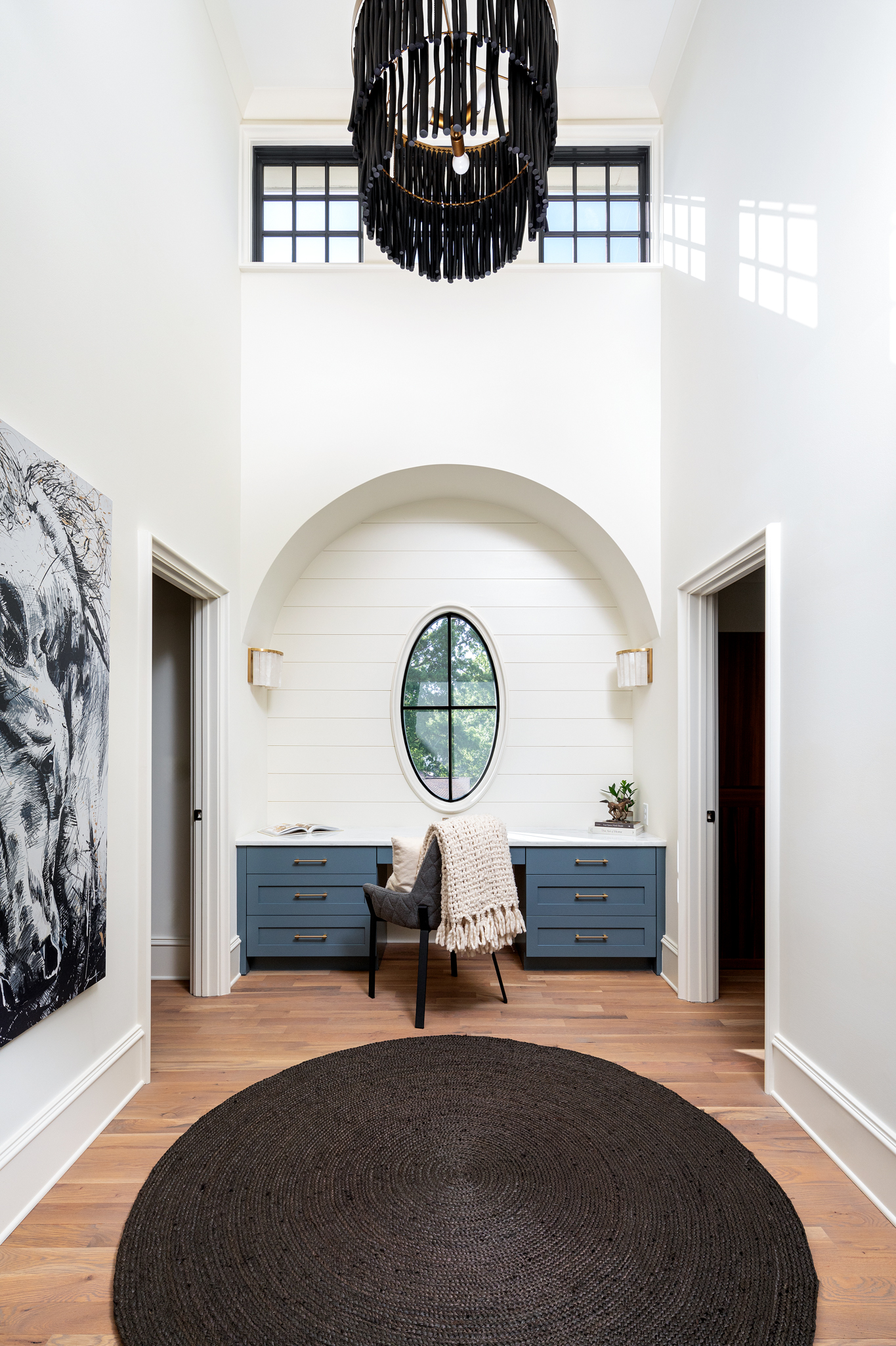 A quiet spot to sit and think. The arched niche, oval window, and statement chandelier make this little desk nook one of our favorite corners in the home. 🖤