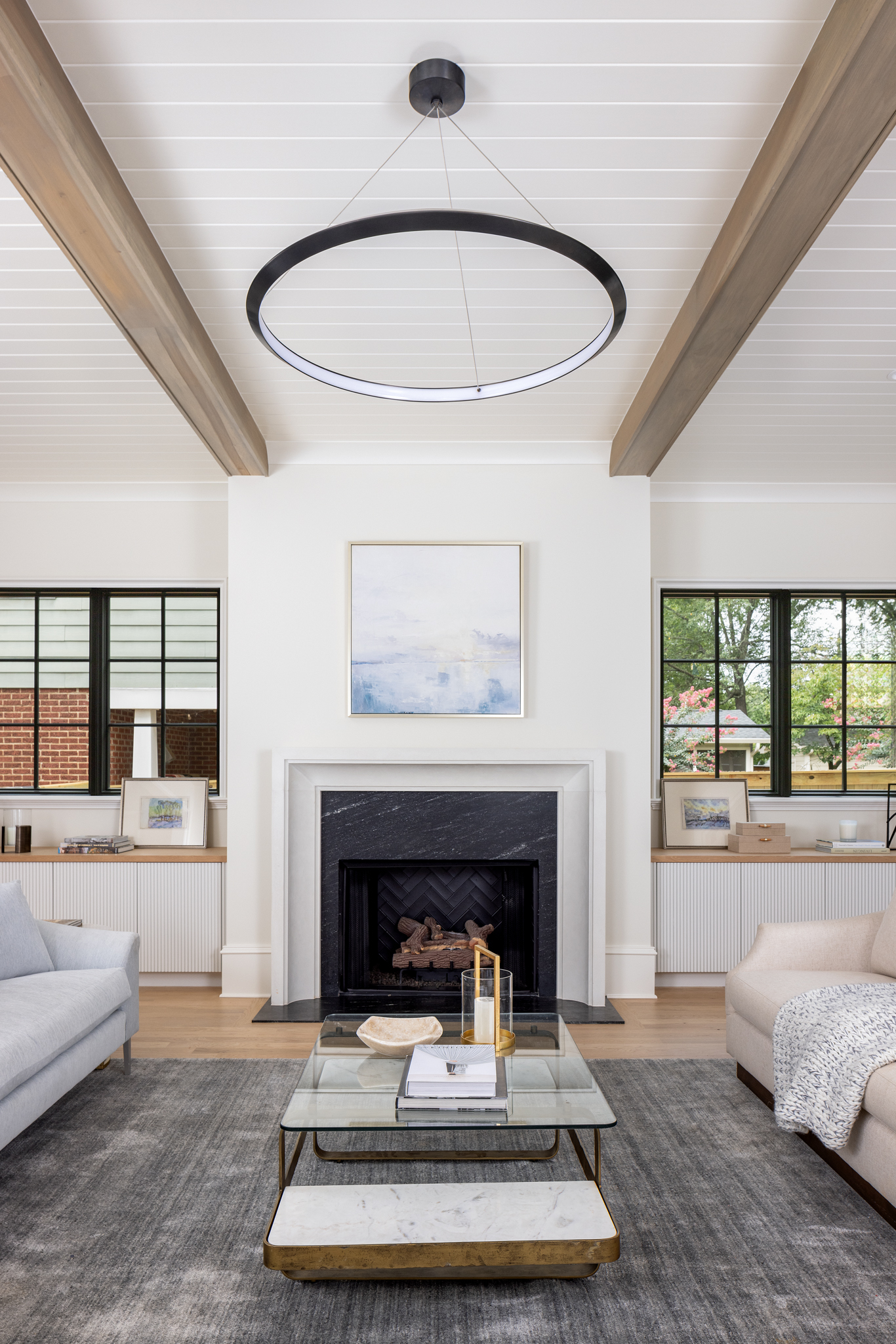 Modern living room with exposed ceiling beams, tongue-and-groove paneling, white oak floors, and a clean-lined fireplace.