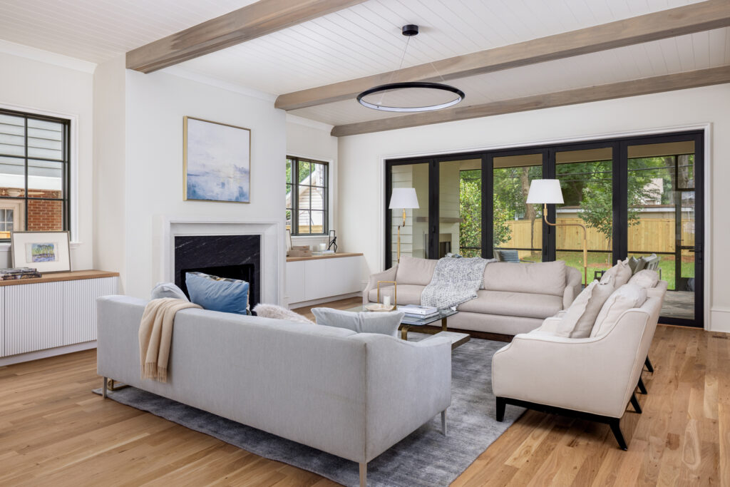 Open-concept living room connected to dining and kitchen areas with white oak flooring and custom built-ins beneath the windows.