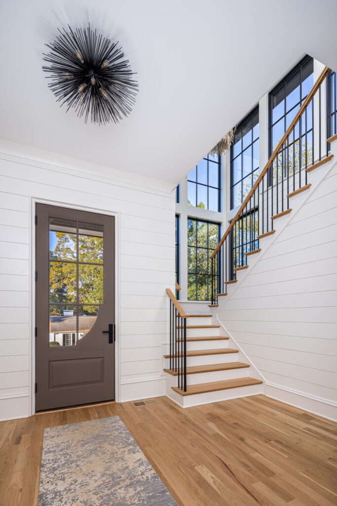 Warren plan front entry with white oak staircase, black iron balusters, and modern chandelier