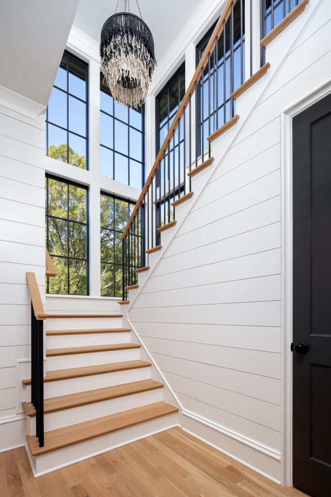 Two-story foyer staircase in Warren plan with shiplap walls and oversized black windows